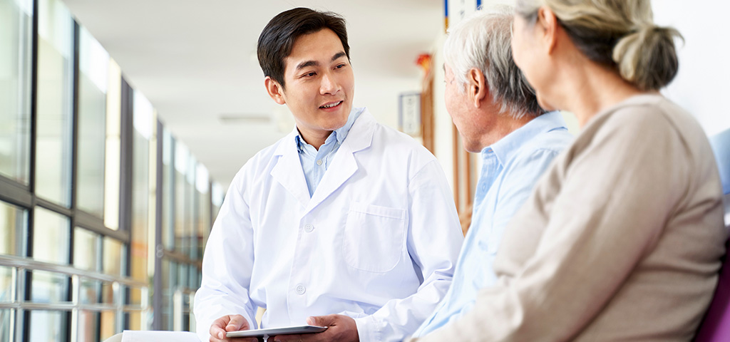 Young asian doctor talking to senior couple patients in hospital hallway